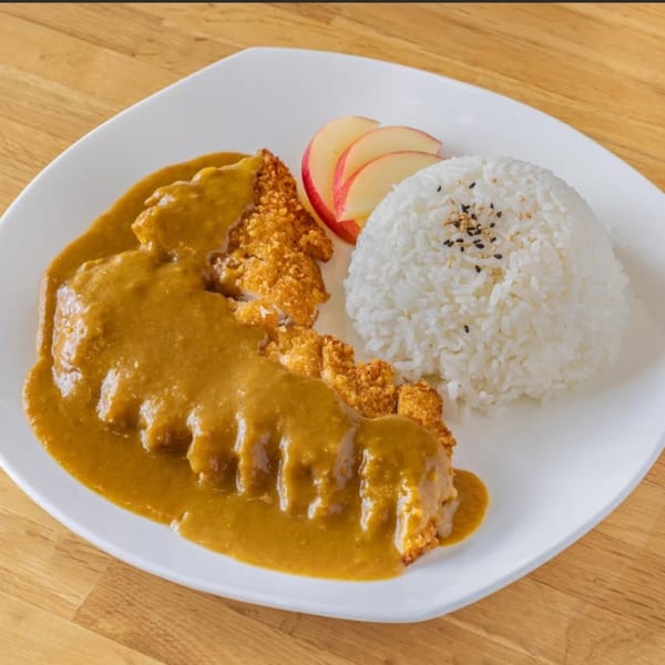 Japanese chicken katsu curry with white rice and sliced apples on a white plate.