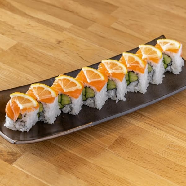 A black rectangular plate holds eight salmon and cucumber sushi rolls, each topped with a lemon slice.