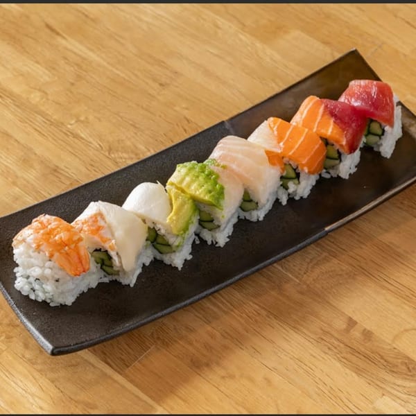 A black rectangular plate holds a row of colorful sushi rolls on a wooden table.